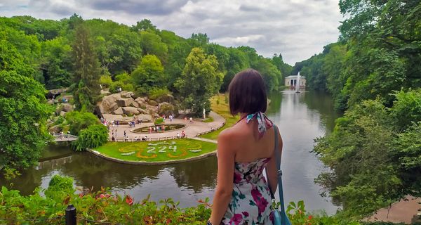 Frau, schaut herunter auf einen Park mit einem großen Teich.