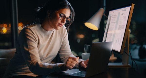 Junge Frau sitzt im Dunkeln im Büro und arbeitet am Computer.