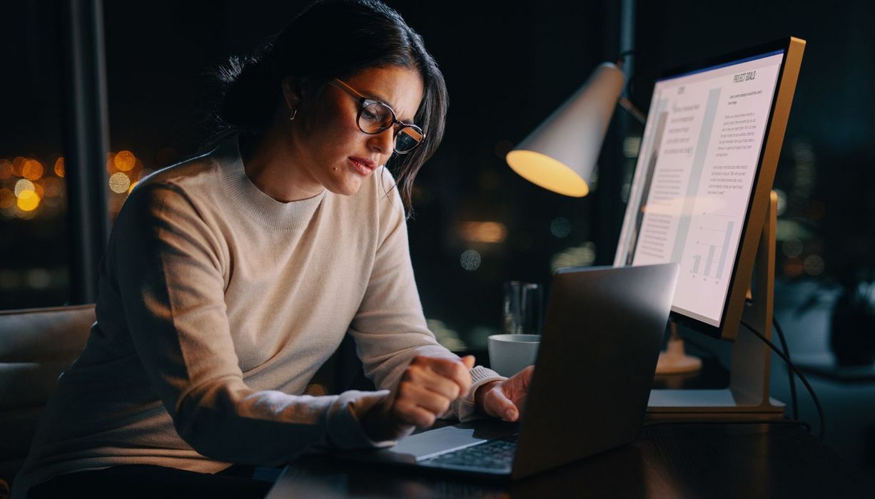 Junge Frau sitzt im Dunkeln im Büro und arbeitet am Computer.