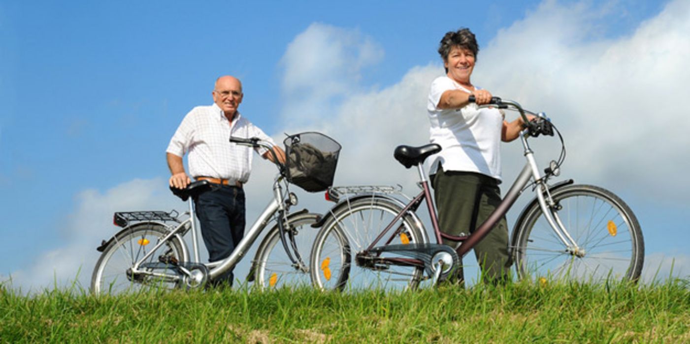 Senioren-Paar, das Fahrräder über eine Wiese schiebt