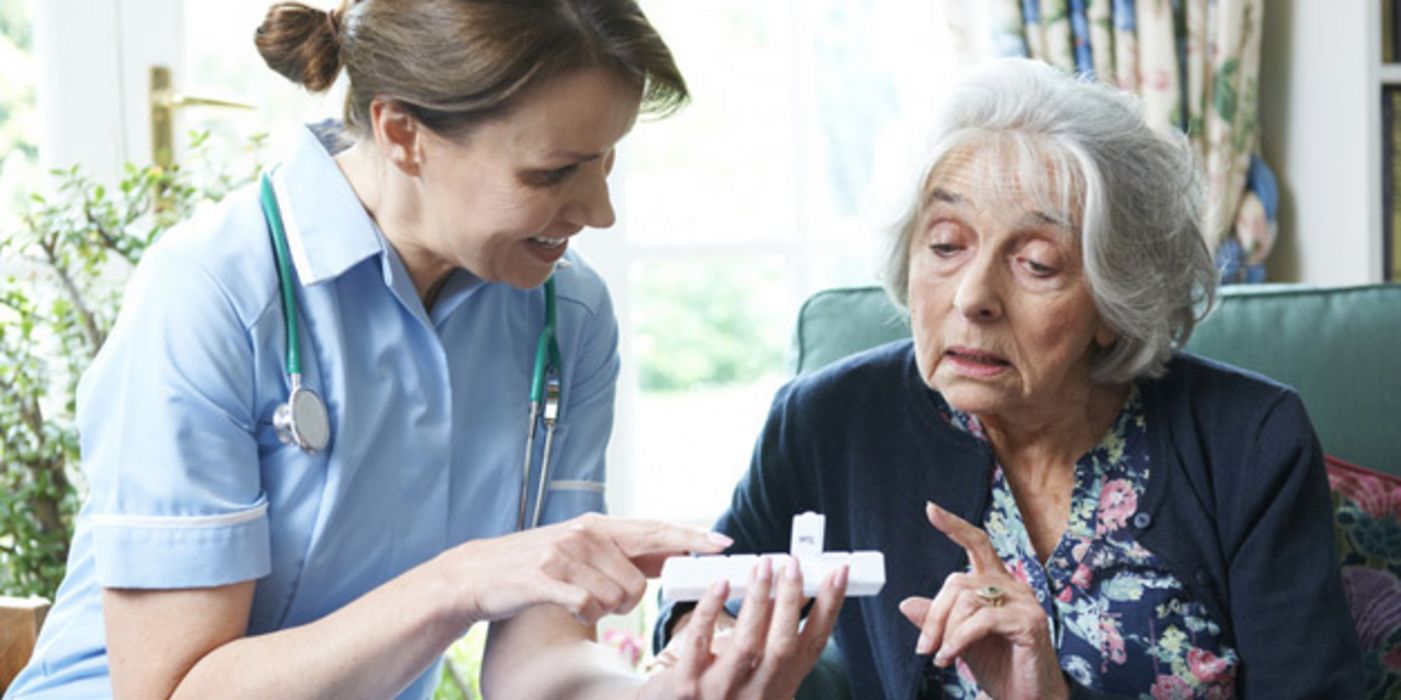 Seniorin bekommt von Pflegerin die Tabletteneinnahme mit einer Dosette erklärt