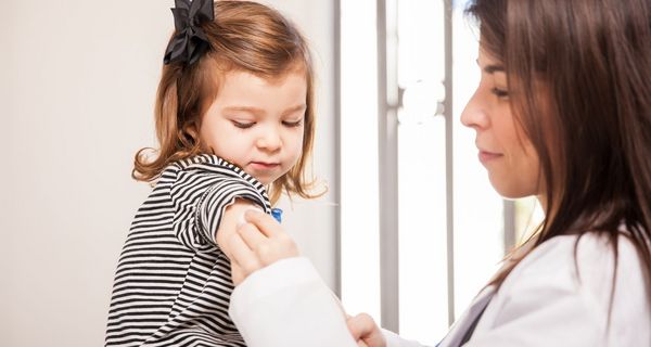 Eine Ärztin desinifiziert den Oberarm eines kleinen Mädchens, das etwa 1,5 Jahre alt ist.