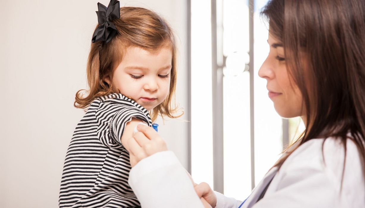 Eine Ärztin desinifiziert den Oberarm eines kleinen Mädchens, das etwa 1,5 Jahre alt ist.