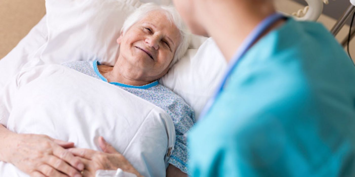 Lächelnde ältere Frau im Krankenhausbett, sie bekommt von einer Ärztin die Hand gehalten