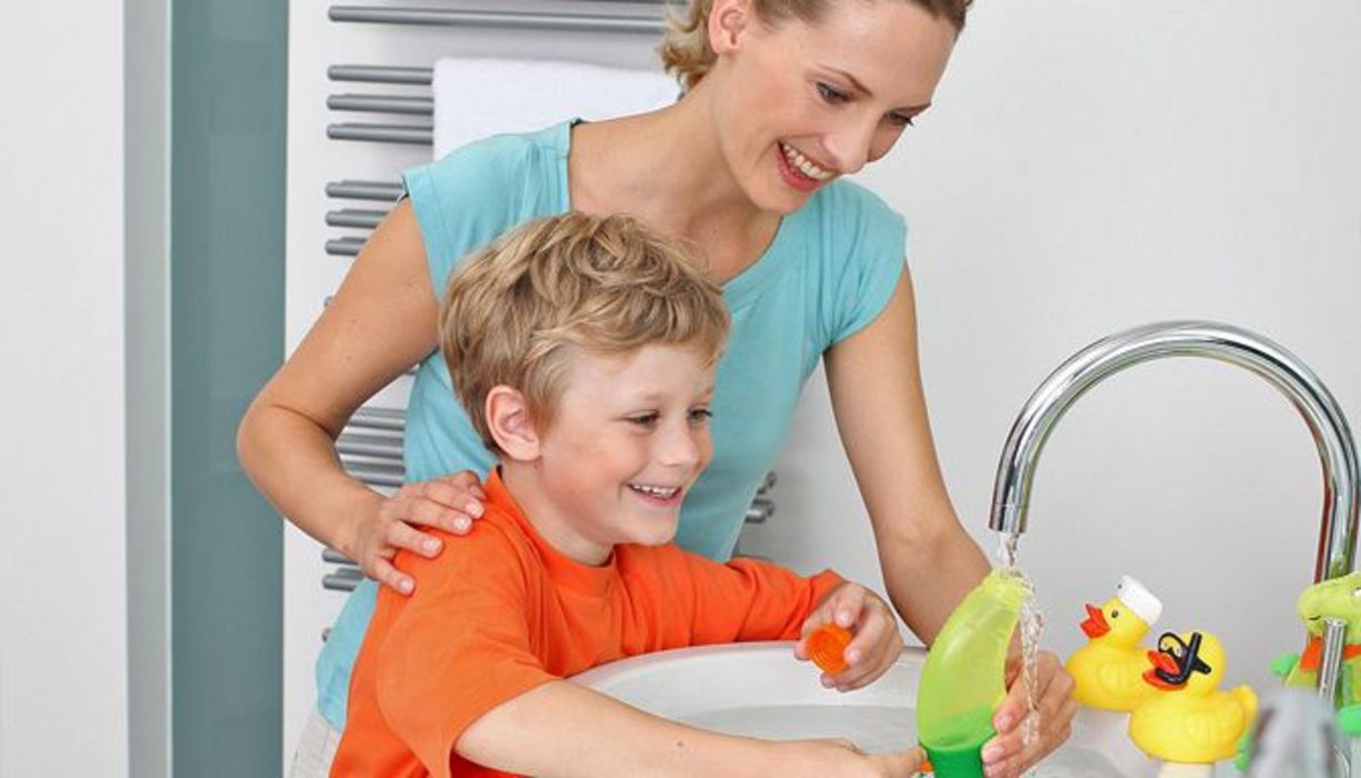 Mutter mit Sohn am Waschbecken beim Befüllen einer Nasendusche