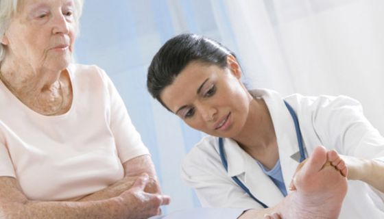 Jüngere Ärztin untersucht bei Seniorin rheumatisch geschwollenen Fuß und Fußgelenk