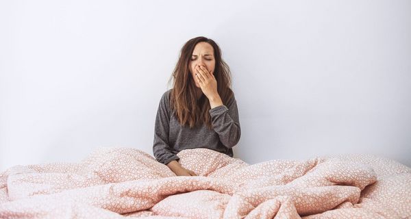 Junge Frau, gähnt, sitzt aufrecht im Bett.