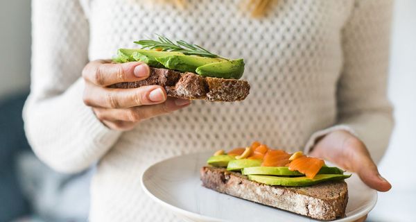 Frau, hat zwei Brote mit Avocado in der Hand.