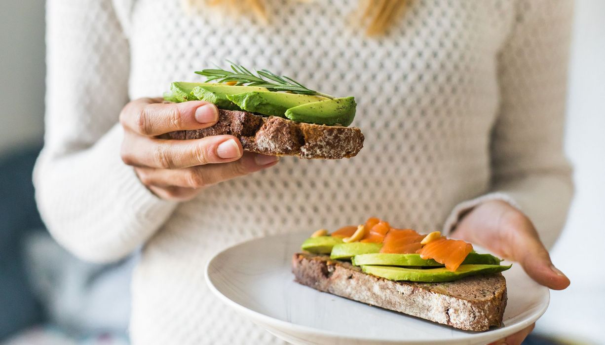 Frau, hat zwei Brote mit Avocado und Lachs.