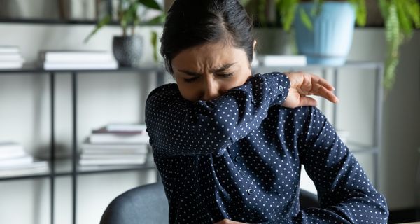 Frau, hustet in ihren Ellenbogen und sitzt im Büro.