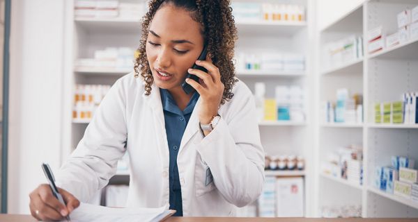 Apothekerin am Telefon, die sich mit einer Hand etwas notiert.