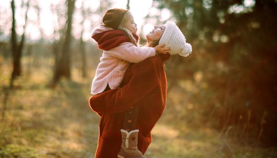 Mutter, hat Tochter auf dem Arm, draußen im Wald.