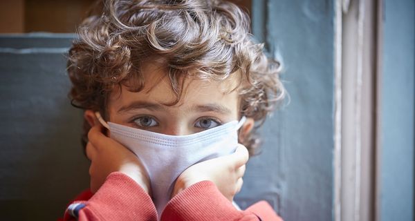 Kind mit Maske, stützt Kopf in die Hände.