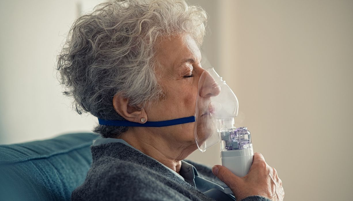 Eine ältere Frau inhaliert mithilfe einer Maske