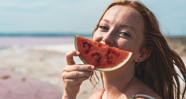 Frau, hält sich eine Wassermelone vor den Kopf.