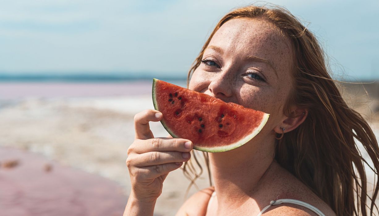 Frau, hält sich eine Wassermelone vor den Kopf.