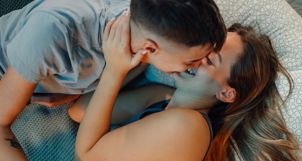 Jugendliches Paar küsst sich im Bett. Beide tragen Kleidung.