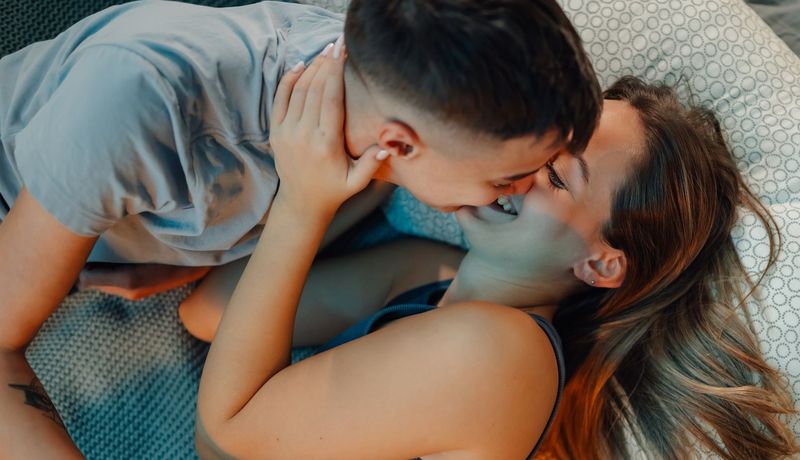 Jugendliches Paar küsst sich im Bett. Beide tragen Kleidung.