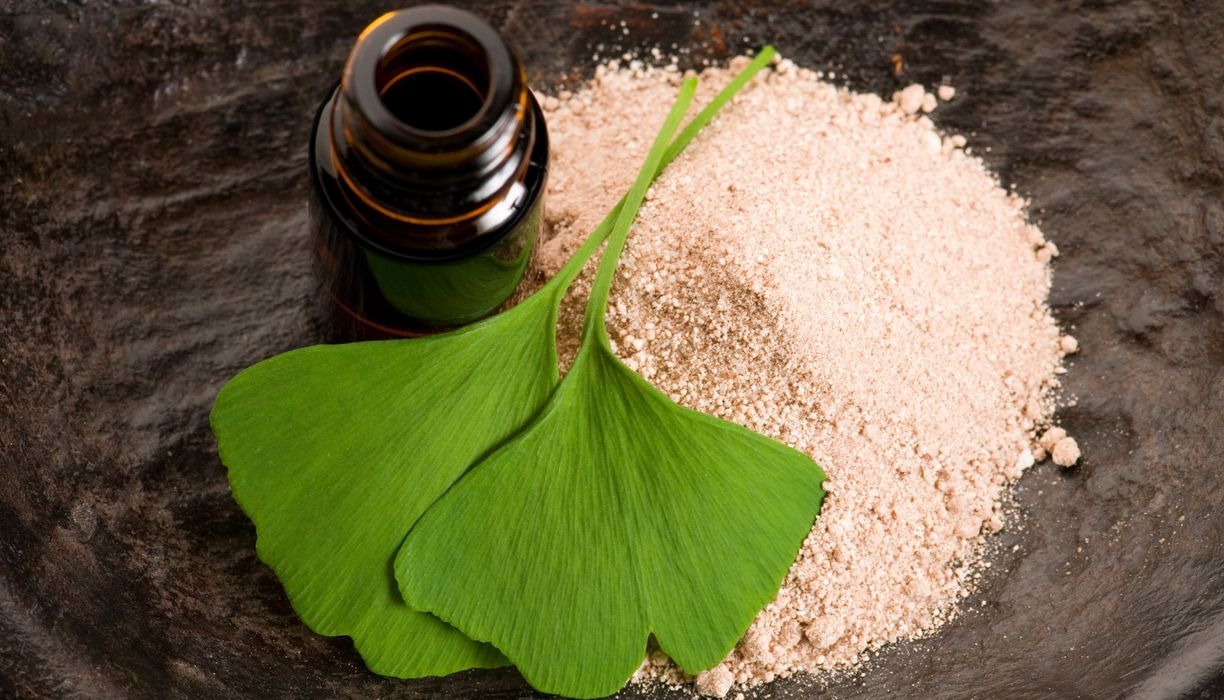 Ginkgo-Blätter neben einer offenen Extrakt-Flasche ohne Ettikett und auf einem Haufen feinen Pulvers.