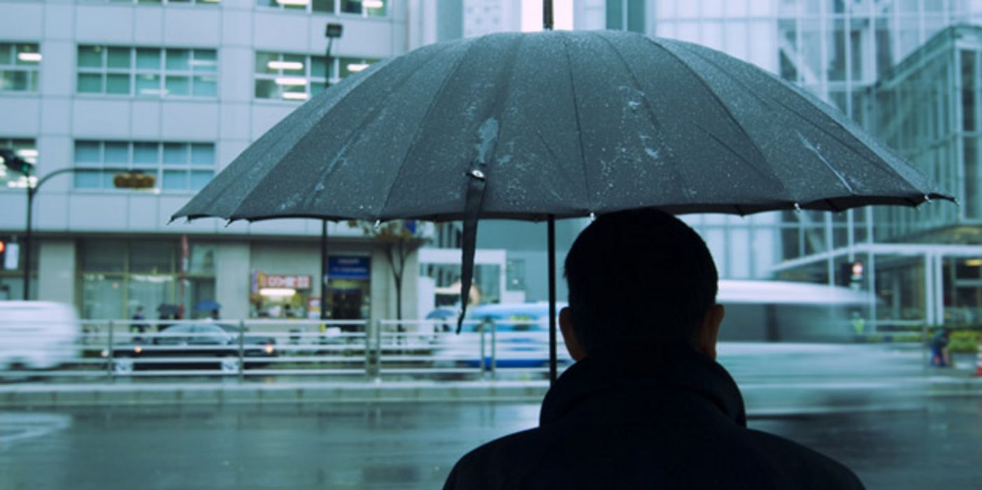 Mann unter Regenschirm bei Schmuddelwetter