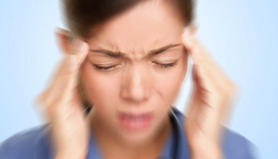 Asiatin hält sich mit schmerzverzerrtem Gesicht die Hände an die Schläfen