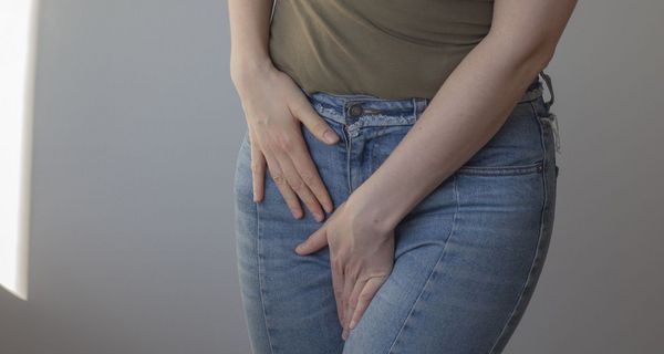 Frau hält wegen Juckreiz und Beschwerden Hände in den Schritt. Sie trägt Kleidung.