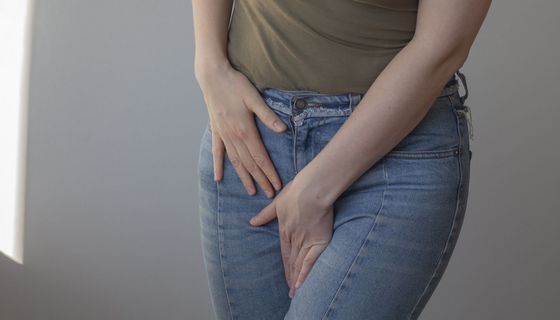 Frau hält wegen Juckreiz und Beschwerden Hände in den Schritt. Sie trägt Kleidung.