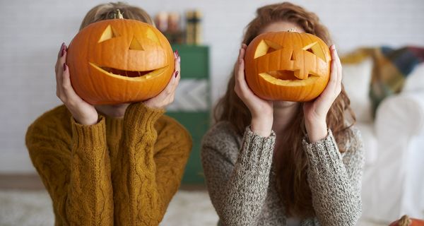 Zwei Frauen, halten sich Kürbisgesichter vor das eigene Gesicht.