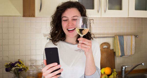 Frau, macht einen Videoanruf und hält ein Glas Wein in der Hand.