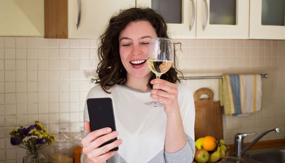 Frau, macht einen Videoanruf und hält ein Glas Wein in der Hand.