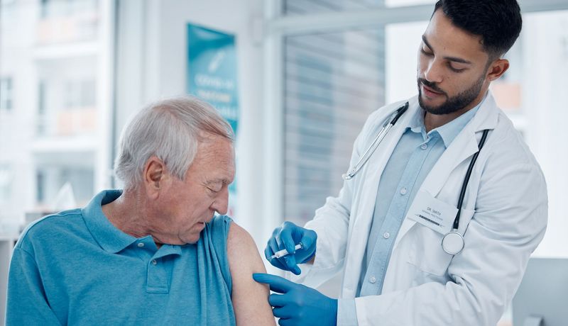 Arzt impft älteren Patienten.
