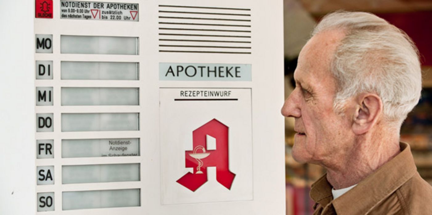 Senior steht vor der Notdienstanzeige einer Apotheke