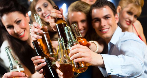 Gruppe junger Leute in Partystimmung hält Flaschen mit alkoholischen Getränken lachend in die Kamera