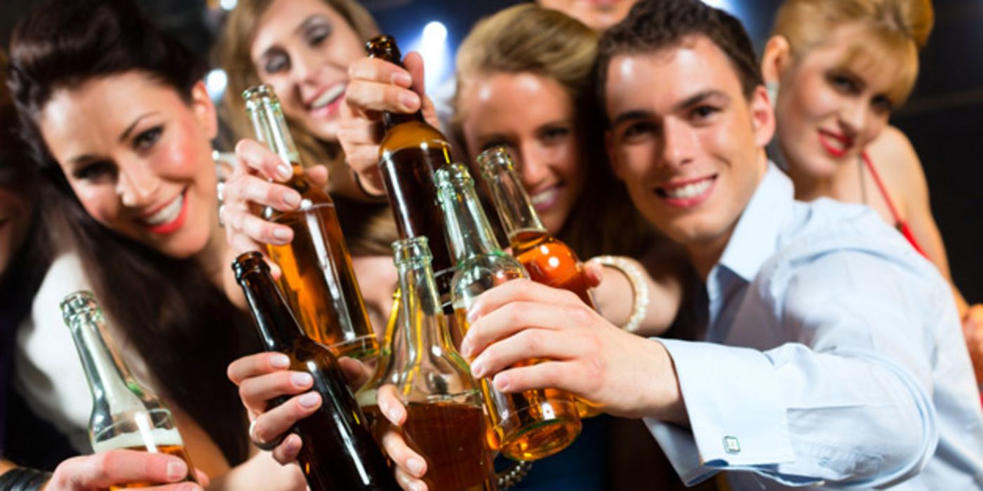 Gruppe junger Leute in Partystimmung hält Flaschen mit alkoholischen Getränken lachend in die Kamera
