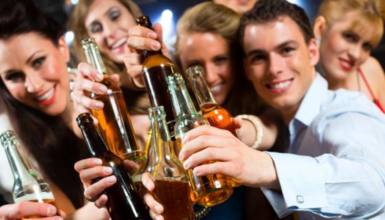 Gruppe junger Leute in Partystimmung hält Flaschen mit alkoholischen Getränken lachend in die Kamera