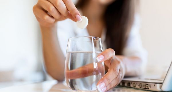 Frau, wirft eine Brausetablette in ein Glas Wasser.