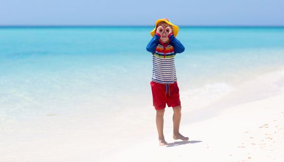 Ein Junge mit spezieller Sonnenschutzkleidung steht an einem Strand.