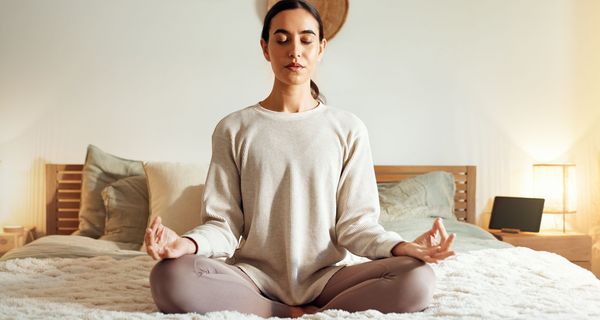 Frau meditiert auf dem Bett.