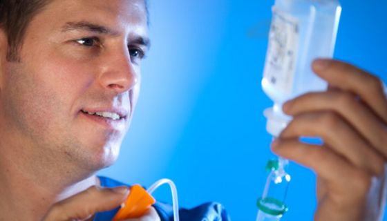 Nahaufnahme Arzt oder Krankenpfleger (blaue Kleidung) schaut auf Infusionsflasche in einer Hand, in der anderen hält er den Infusionsschlauch