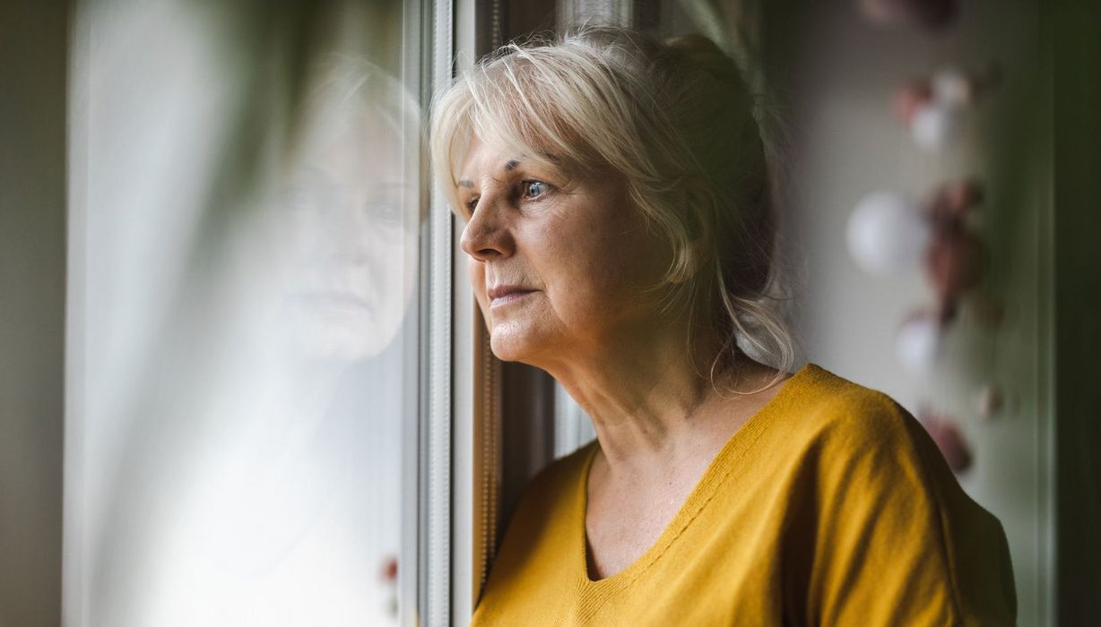 Eine Frau im Alter zwischen etwa 50 und 65 Jahren schaut nervös und angespannt aus dem Fenster.