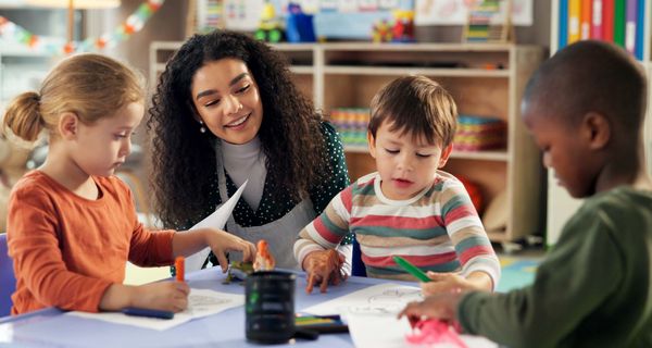 Drei etwa vierjährige Kinder malen unter Aufsicht Bilder.