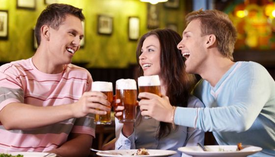 Zwei junge Männer und eine junge Frau stoßen mit Biergläsern an