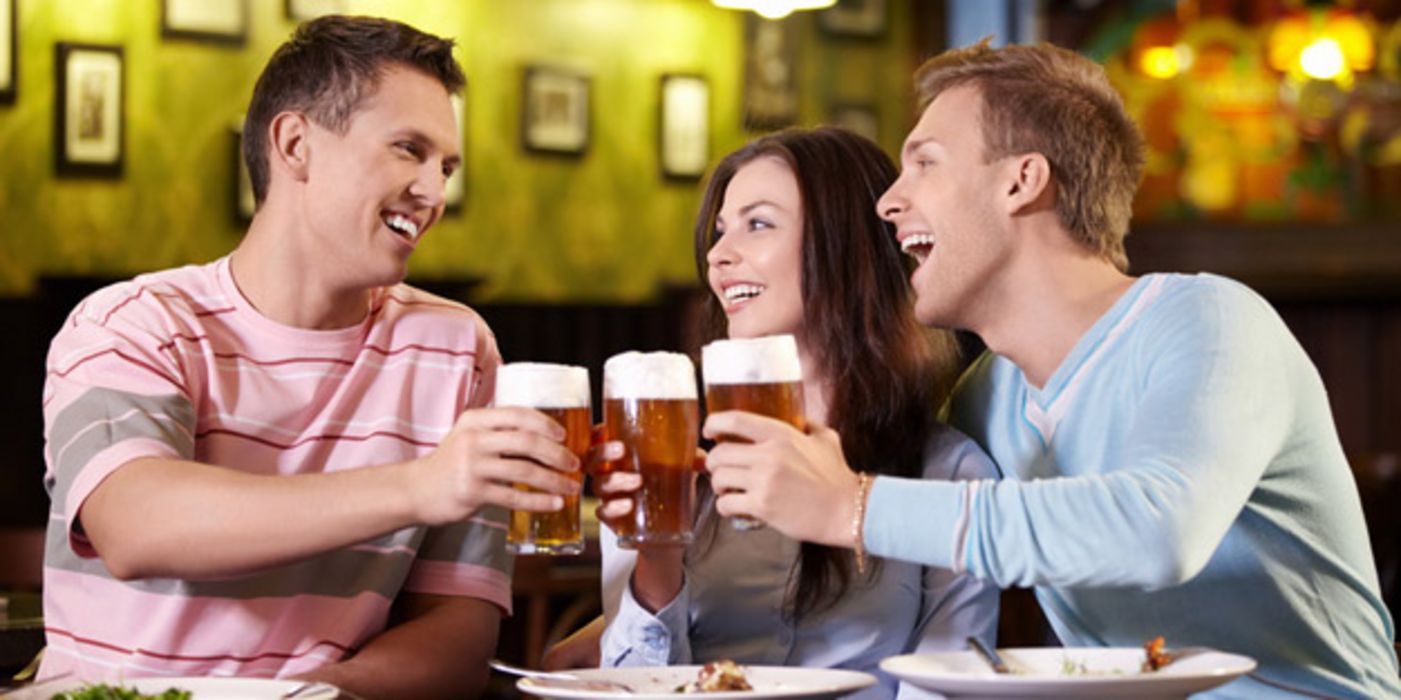Zwei junge Männer und eine junge Frau stoßen mit Biergläsern an