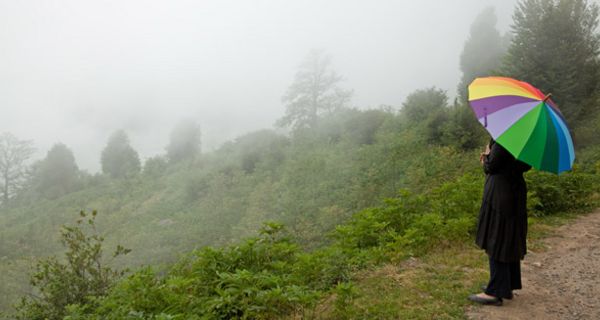 Frau mit buntem Regenschirm steht in nebeliger und hügeliger Landschaft