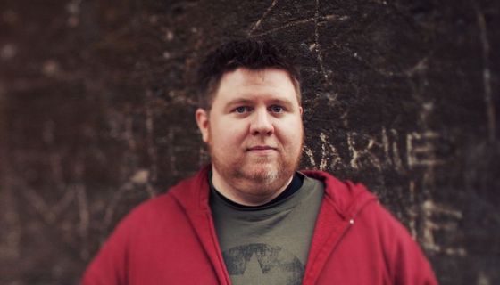 Dicker Mann, steht vor dunkler Wand.