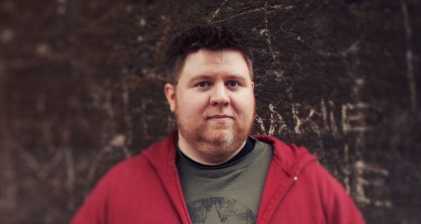 Dicker Mann, steht vor dunkler Wand.