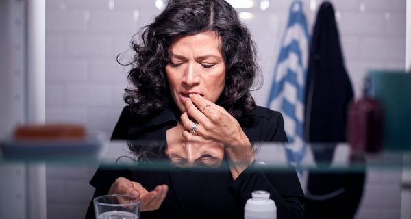 Frau, steht vor einem Spiegelschrank und nimmt Medikamente.