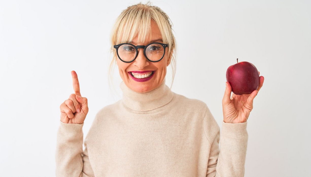 Frau, hält einen Apfel in der Hand und hält einen Finger der anderen Hand nach oben.