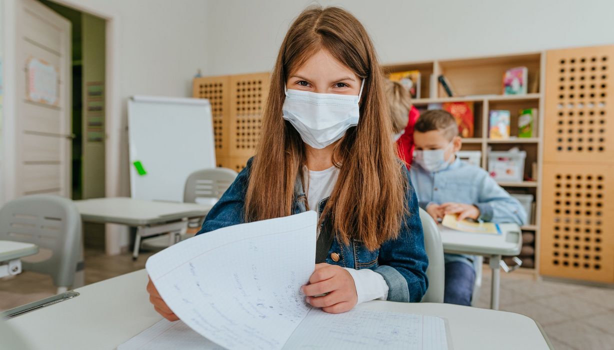 Junges Mädchen mit OP-Maske im Klassenzimmer.