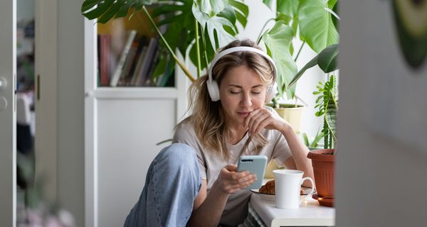 Junge Frau, sitzt zu Hause mit Kopfhörern und hört Musik.